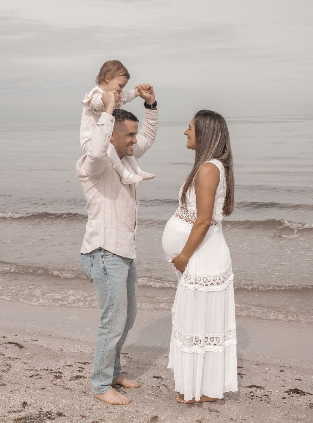 Family walking and embracing together along a peaceful beach shore in coordinated white outfits.