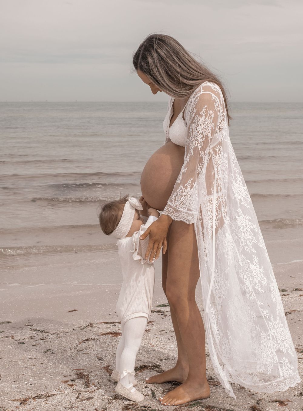 Mother and child in white outfits sharing tender moments together on a misty beach.