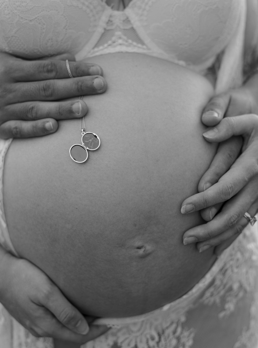 Black and white maternity photo of pregnant belly with wedding rings and hands cradling bump.