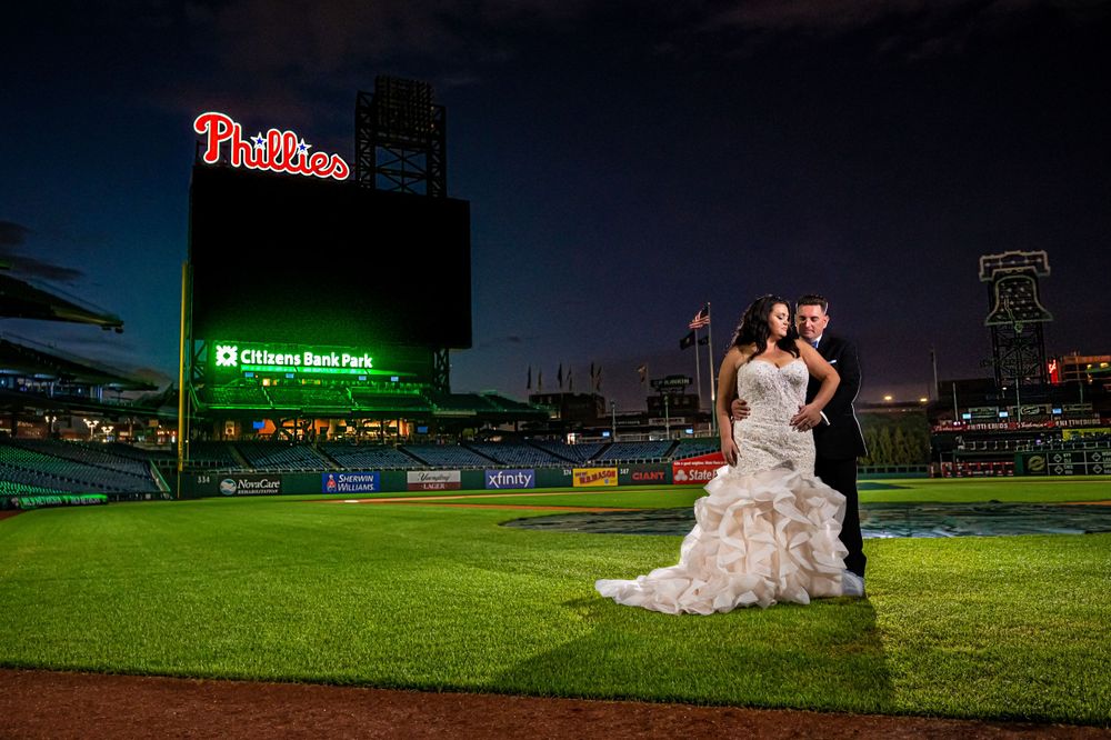 Evening wedding portrait on baseball field with Phillies stadium scoreboard illuminated in background in Citizens Bank Park.