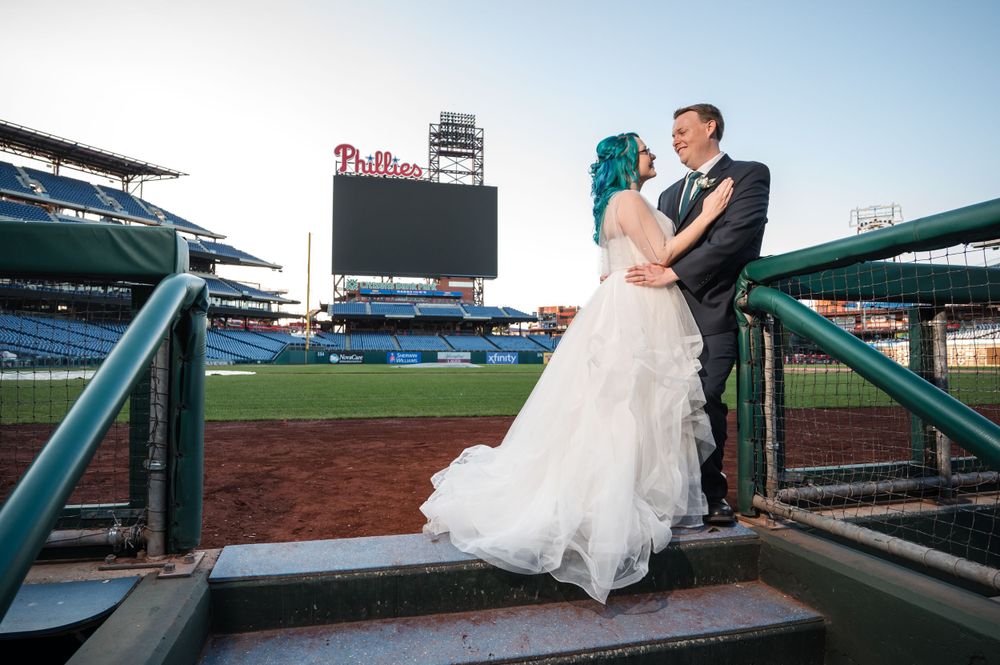 Wedding couple poses on dugout steps at Citizens Bank Park with Phillies sign visible.
