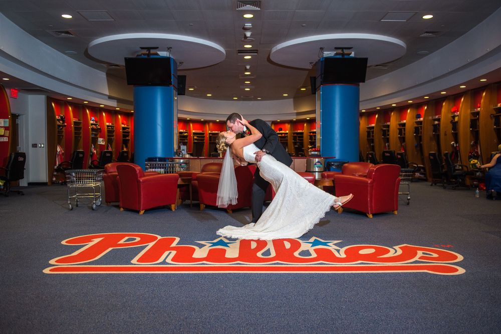 Romantic dip pose in Phillies baseball team locker room with red carpeting and lockers in Citizens Bank Park.