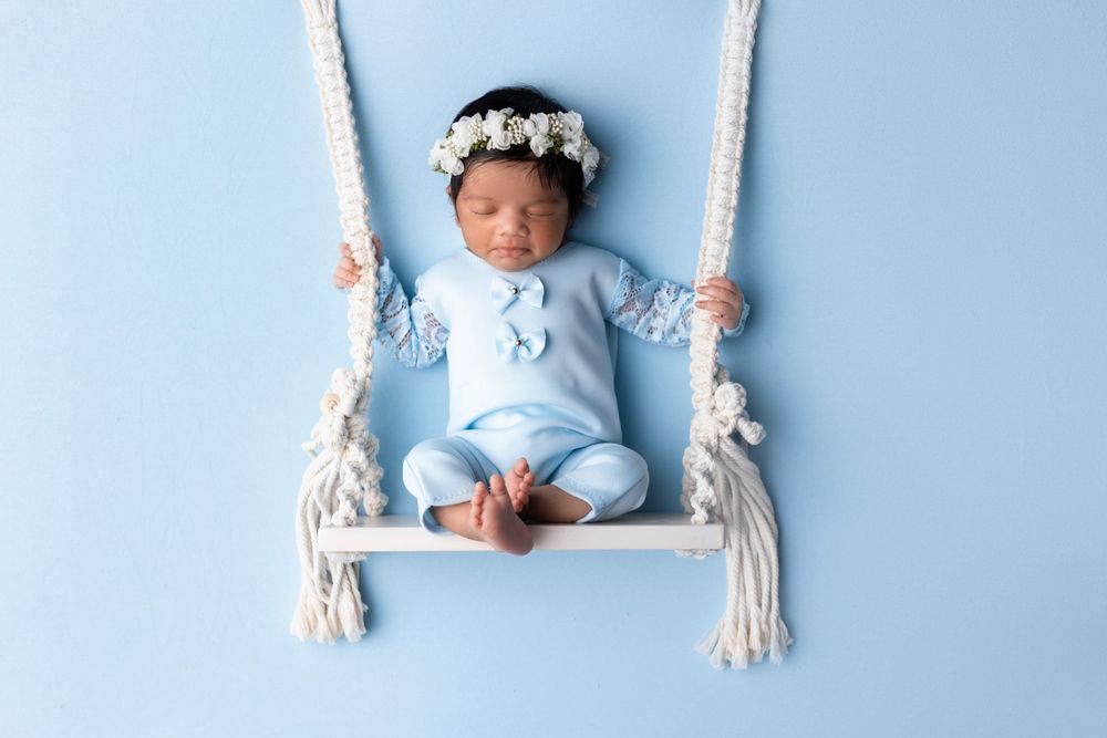 Sleeping newborn in blue outfit on white macrame swing against blue background.