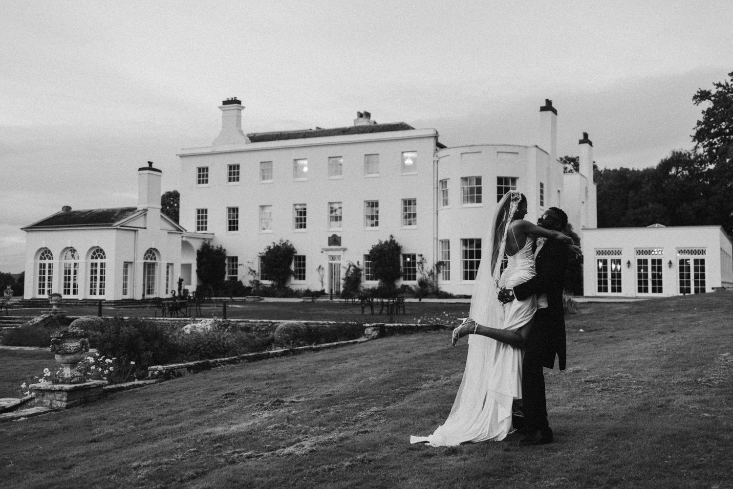 Black and white romantic portrait of couple embracing outside historic mansion.