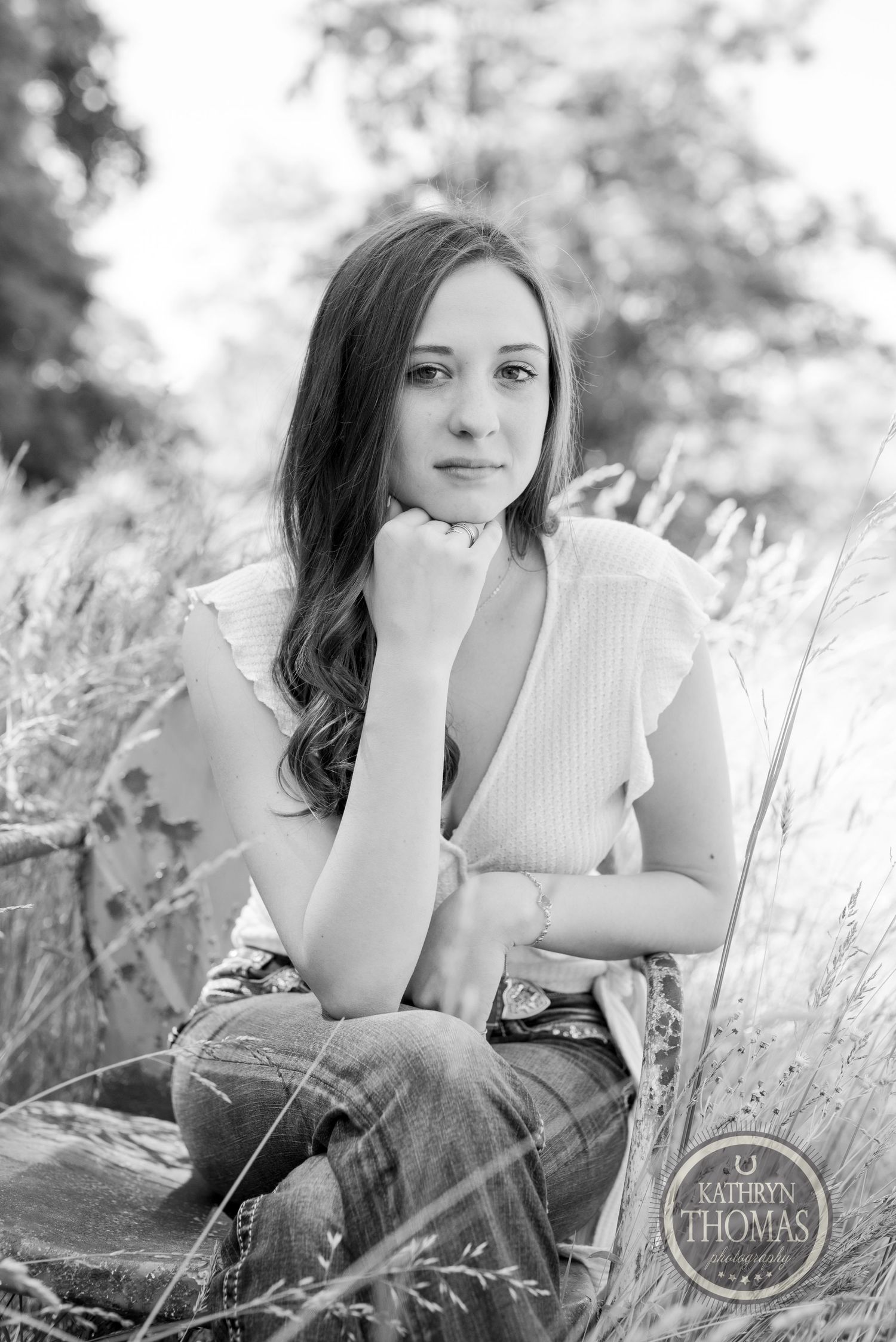 Black and white portrait in tall grass with vintage chair creating dreamy outdoor atmosphere.