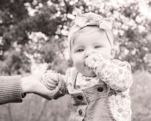 A small child in a knit cardigan and headband reaches out to hold an adult's hand in a black and white photograph.