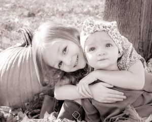 A black and white photo showing a tender moment between two siblings sitting together outdoors.