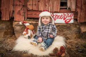 Country western holiday photo with plaid shirt, white fur rug, and rustic red barn backdrop.