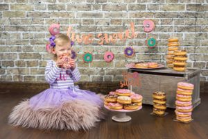 A "Two Sweet" birthday session including a decorated brick wall with cake stands and donuts on wooden table.