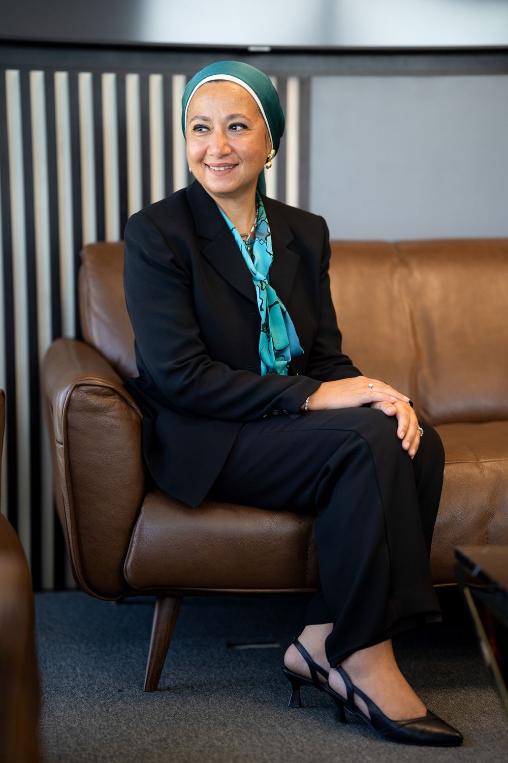Professional portrait on brown leather chair in modern office setting.