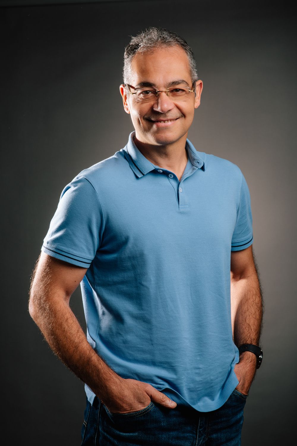 Professional headshot of person in blue polo shirt against dark background with warm lighting.