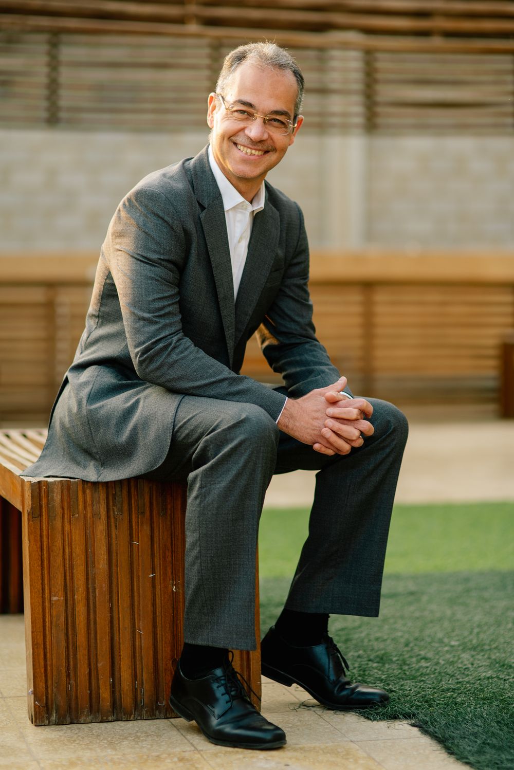 Professional seated portrait outdoors on wooden box wearing grey suit with natural lighting.