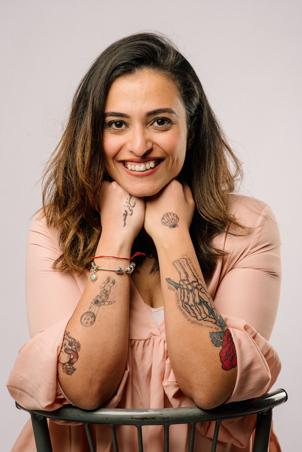 Portrait showing artistic tattoos while wearing peach-colored blouse against neutral background.