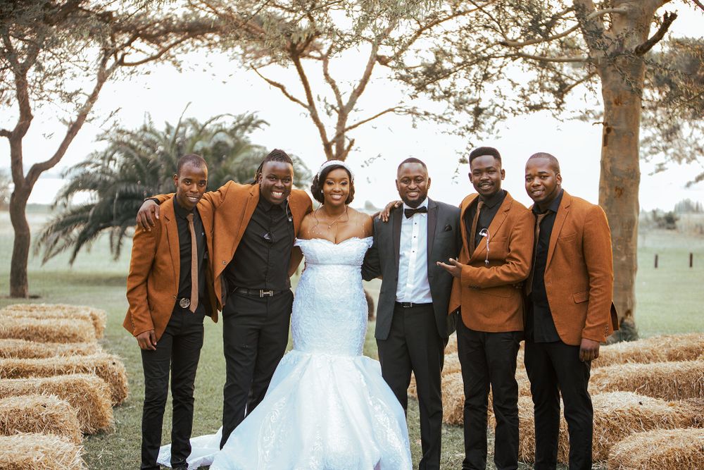 Wedding party in coordinated brown suits posing outdoors with trees in background.
