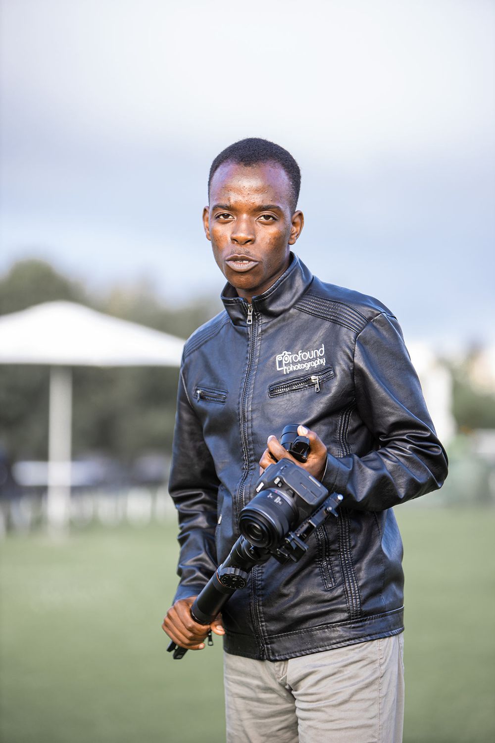 Professional photographer wearing leather jacket holding camera equipment outdoors.