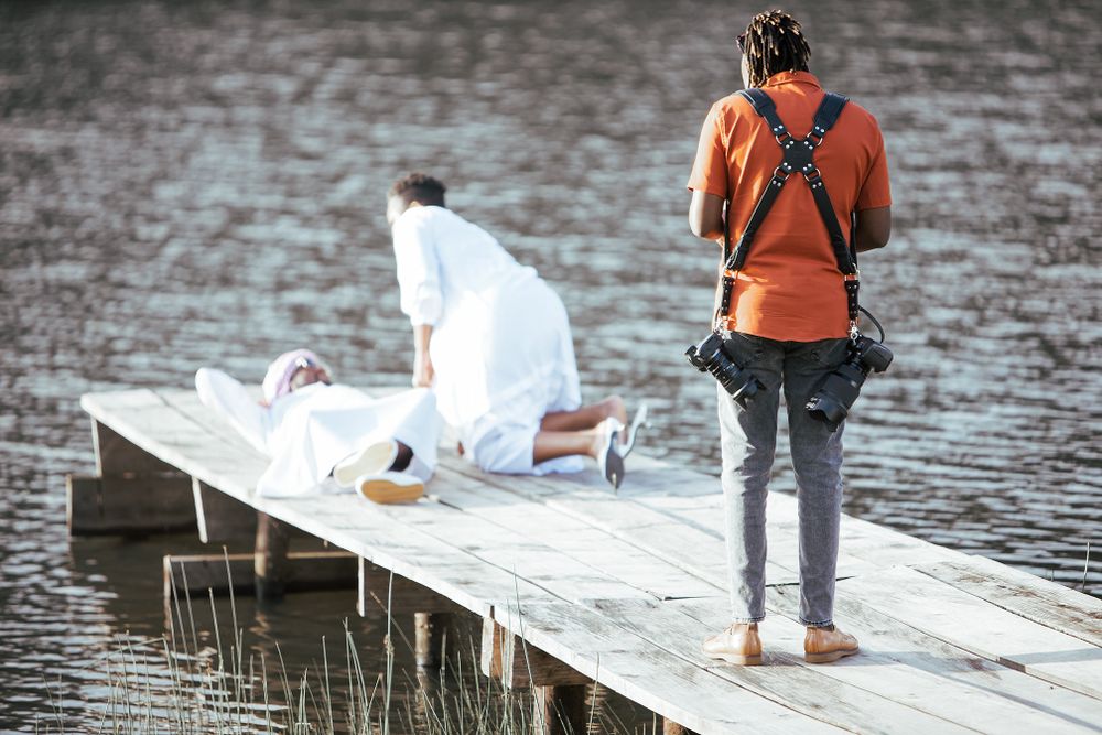 Two photographers working on a wooden dock near water capturing a photoshoot.