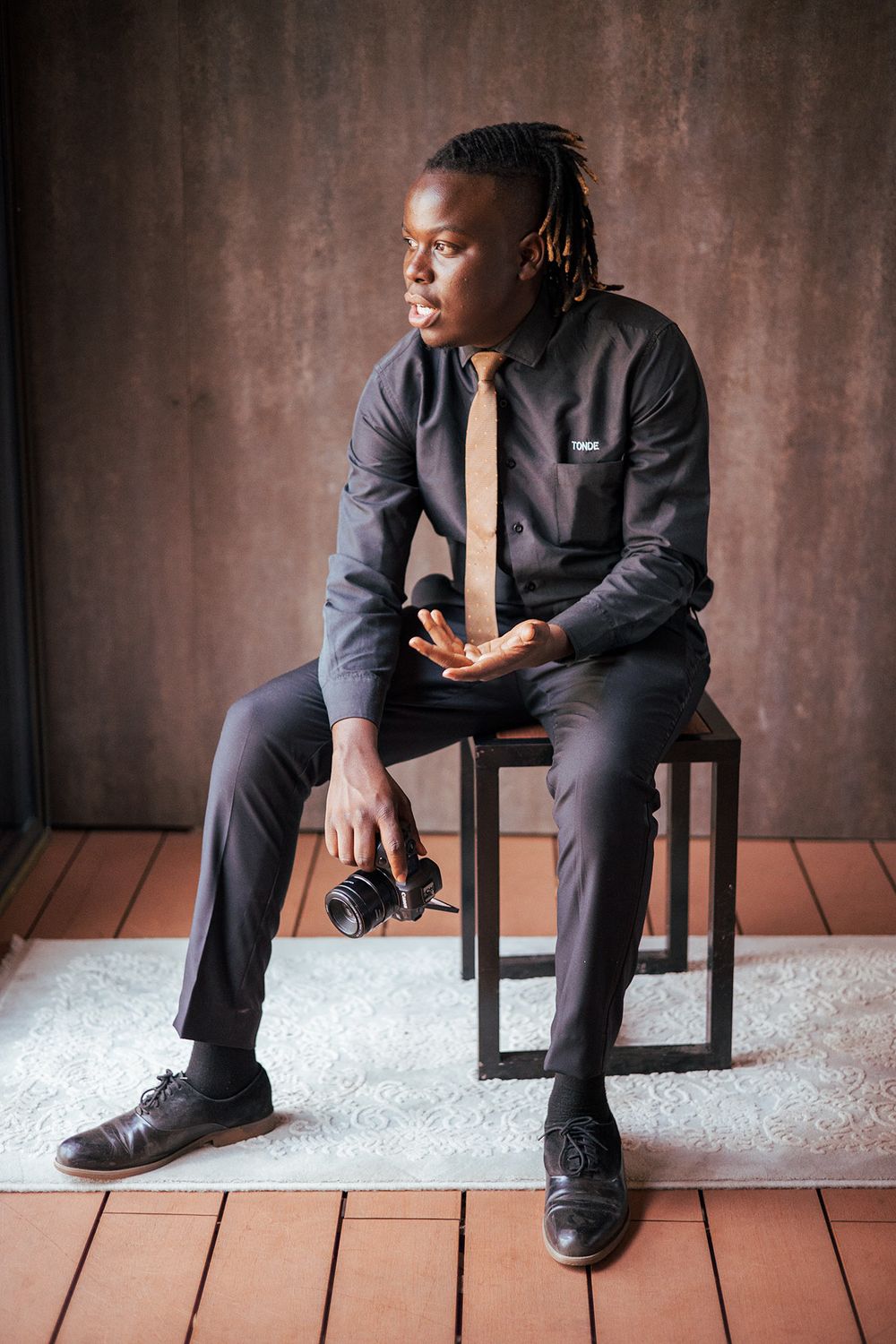 Professional photographer in formal attire sitting with camera equipment in studio setting.