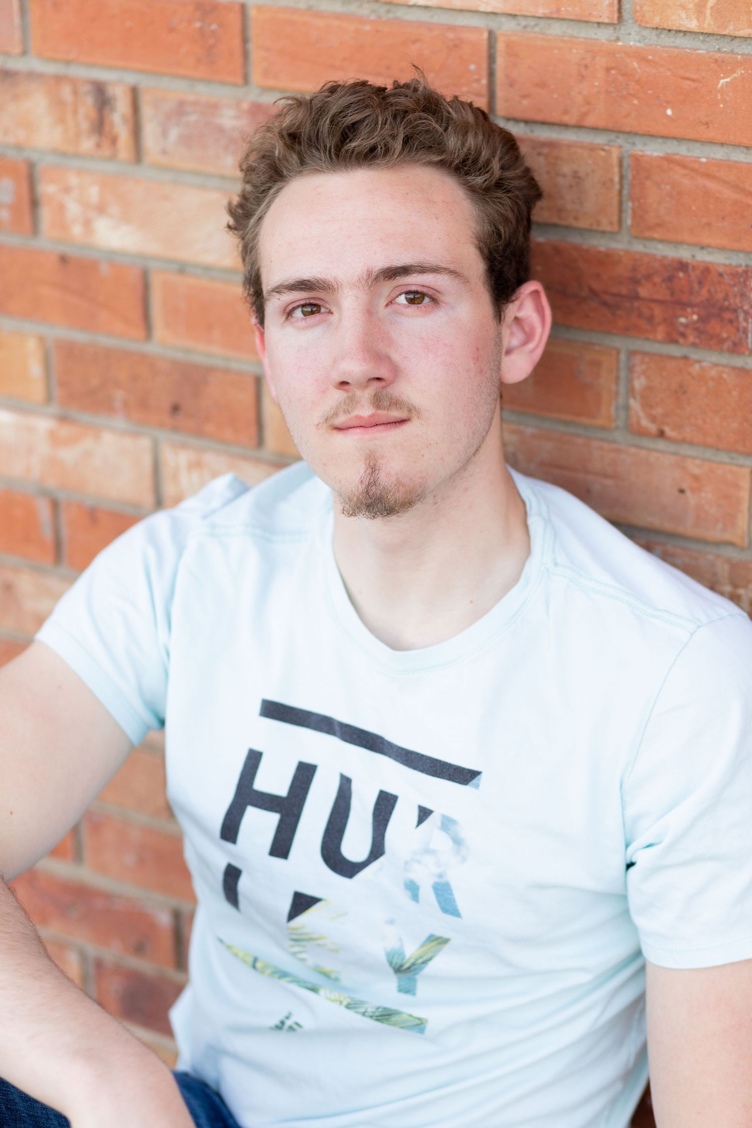 boy sitting against a brick wall lookin at the camera