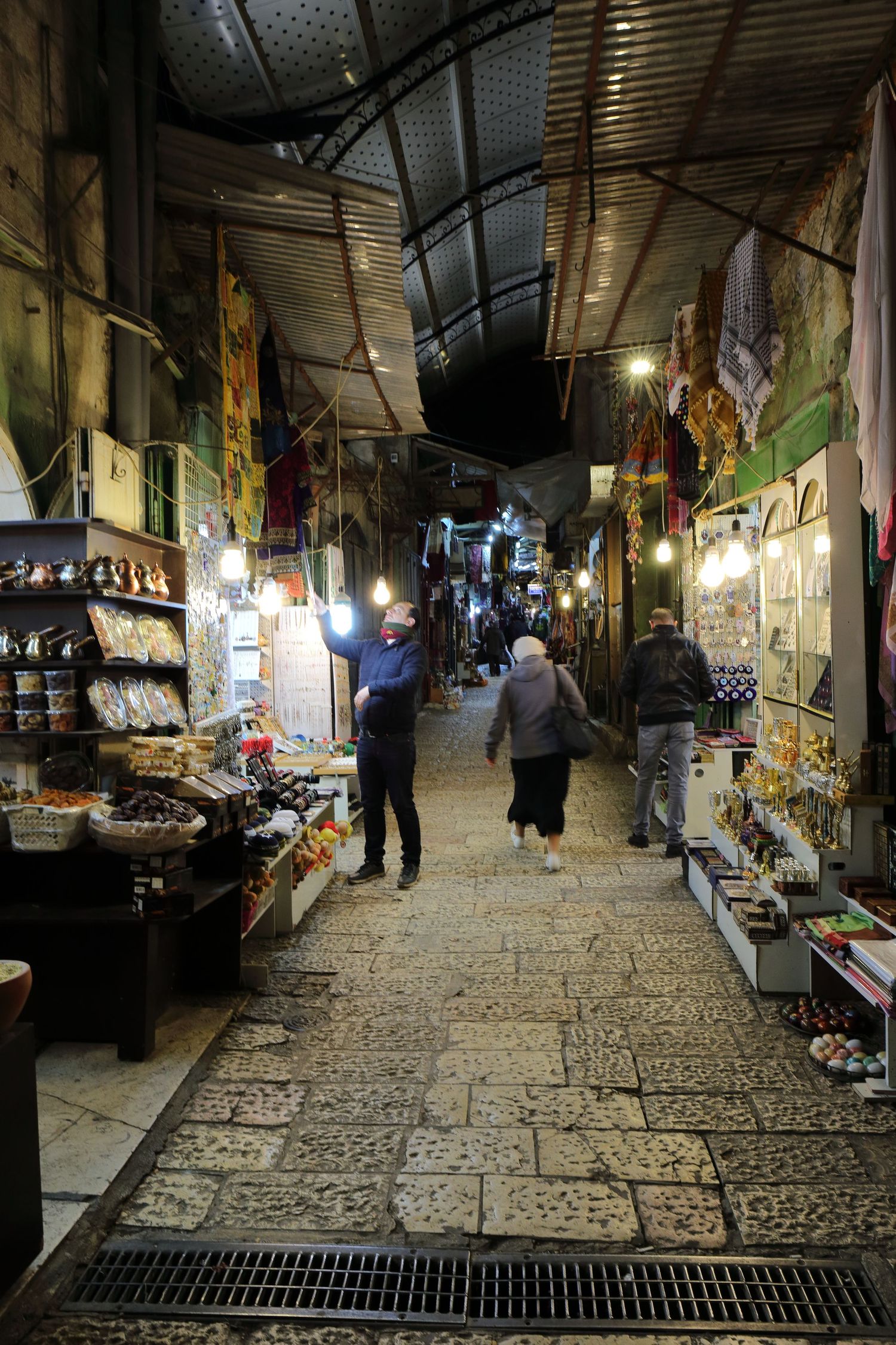Narrow covered marketplace alley with shops and vendors in Jerusalem's Old City.