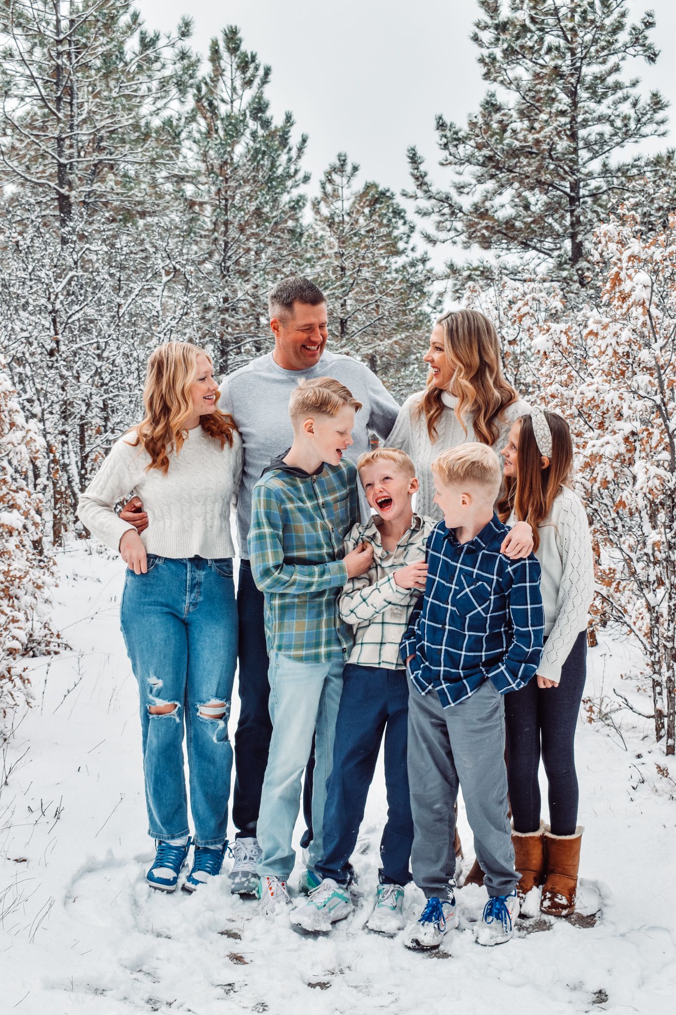 Joyful family of seven posing together in a snow-covered winter pine forest.