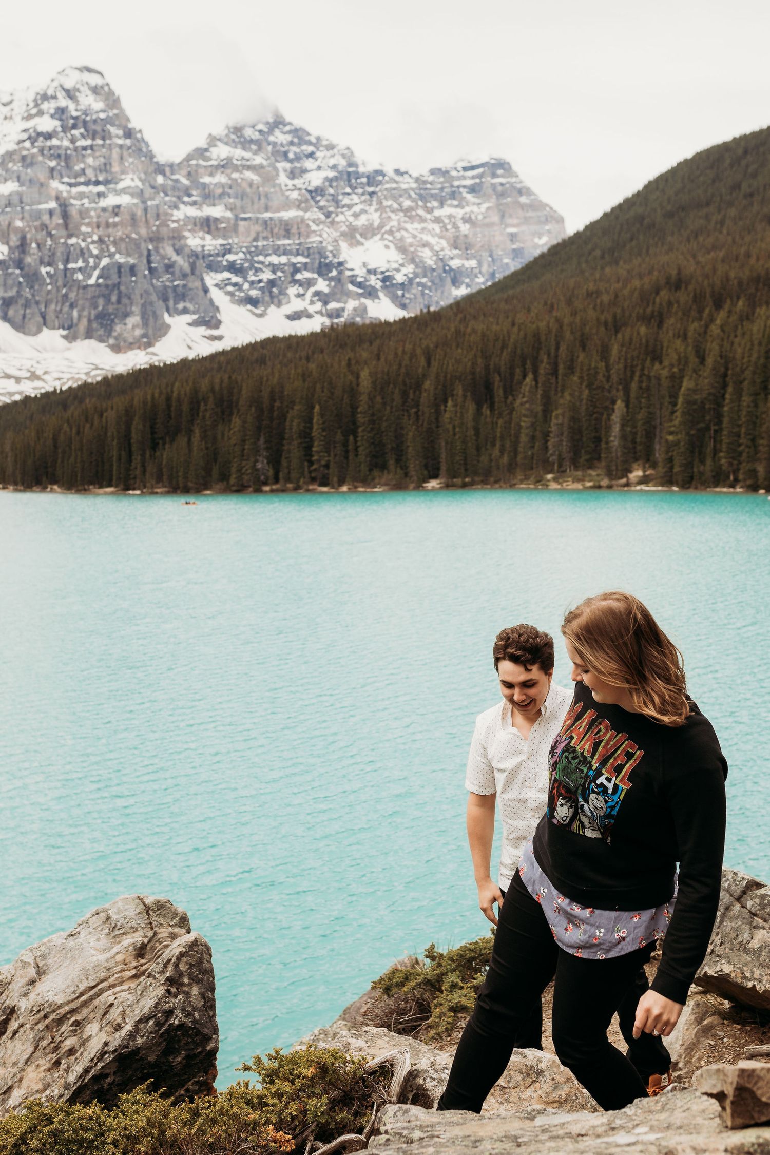 A couple enjoying the stunning view of turquoise waters and snow-covered peaks at Moraine Lake.