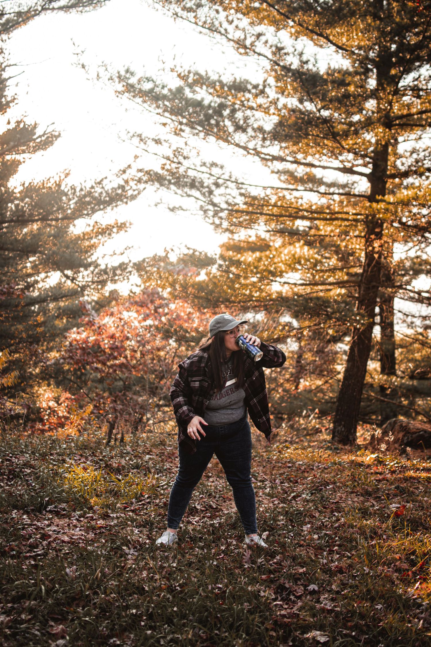 Figure in dark clothing poses energetically among autumn trees with sunlight filtering through branches.