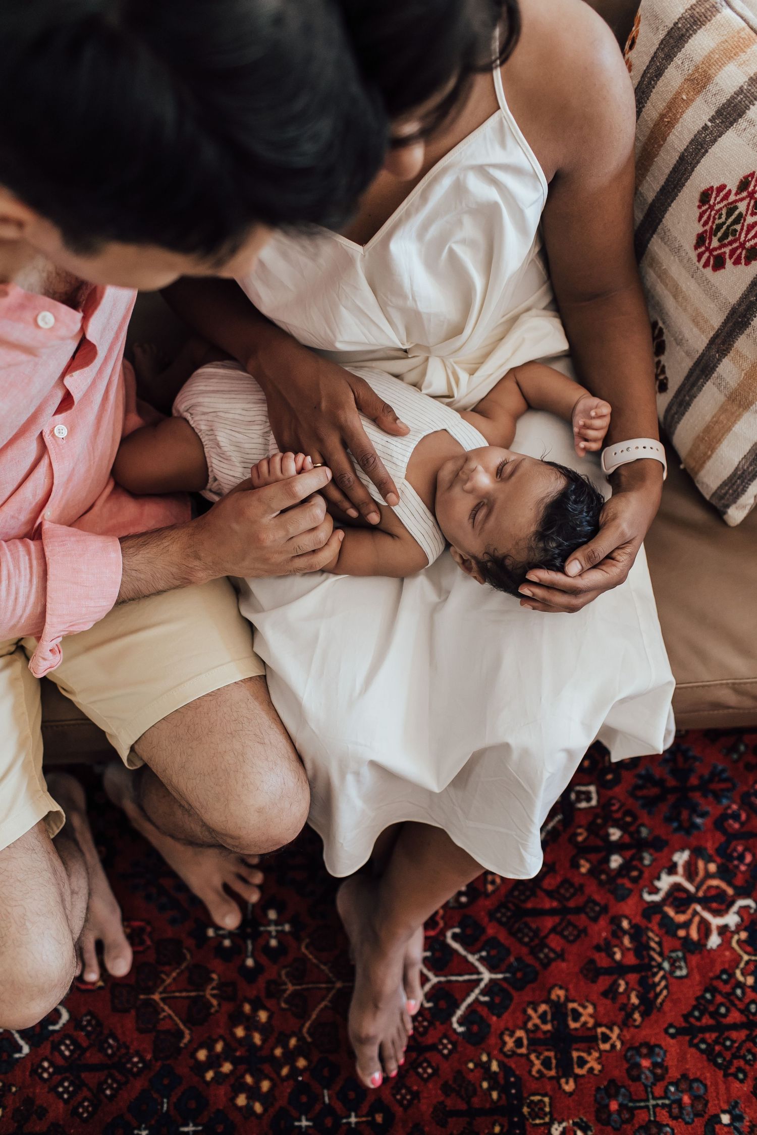 Parents holding newborn baby on colorful rug from above.