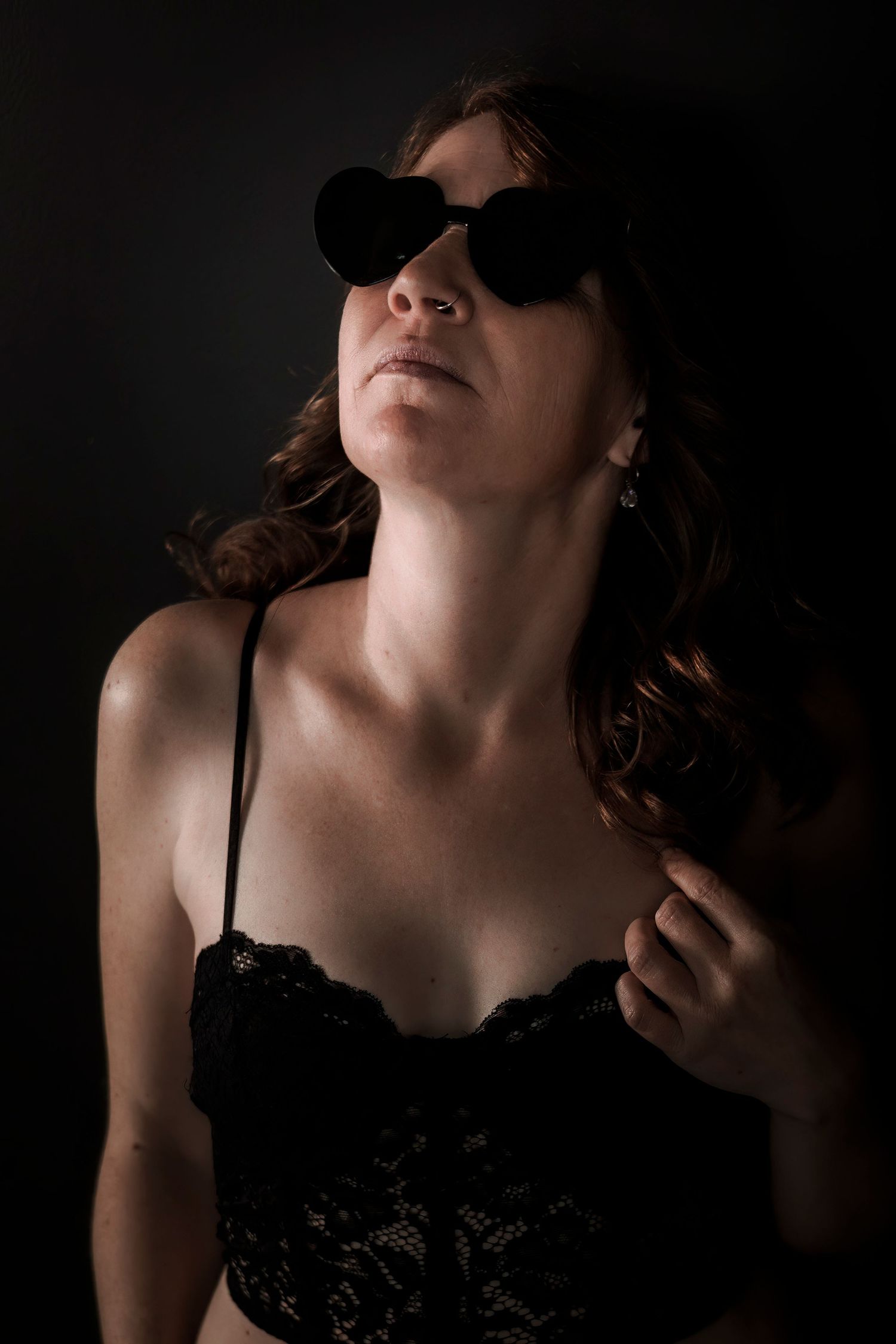 Dramatic portrait with black sunglasses and lace top against dark background.