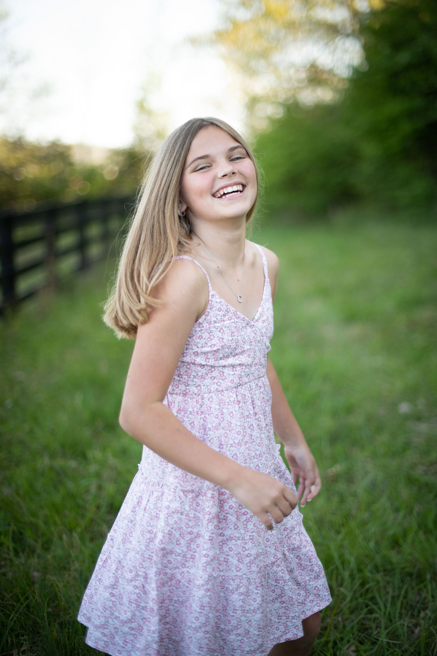 A floral print dress twirls in a sunny outdoor setting with a wooden fence in the background.