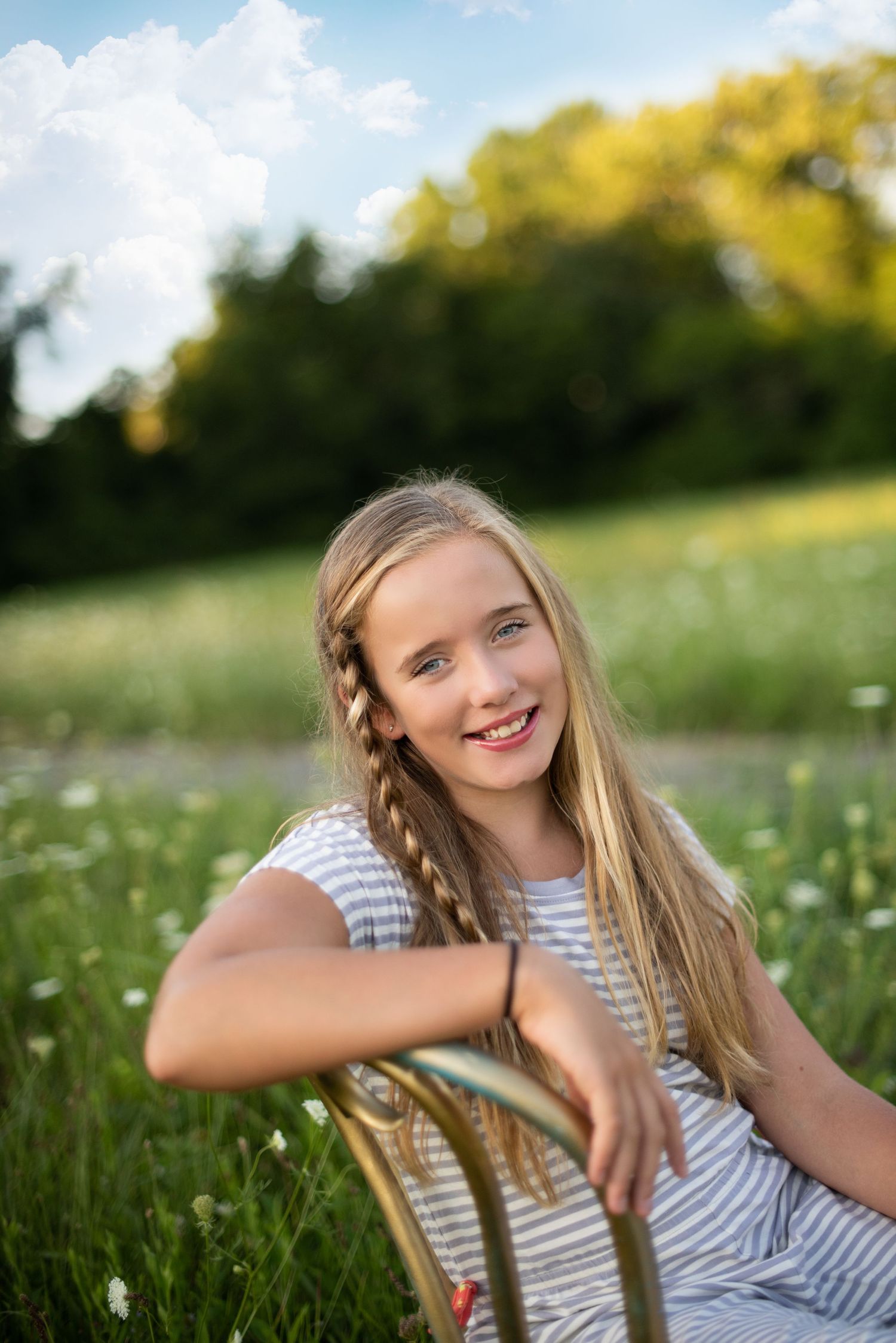 A youth with braided hair sits in a sunny meadow wearing a striped outfit.