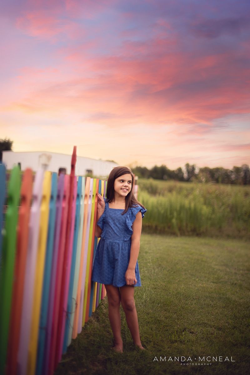 Outdoor photo session at sunset with colorful pencil props against a grassy field.
