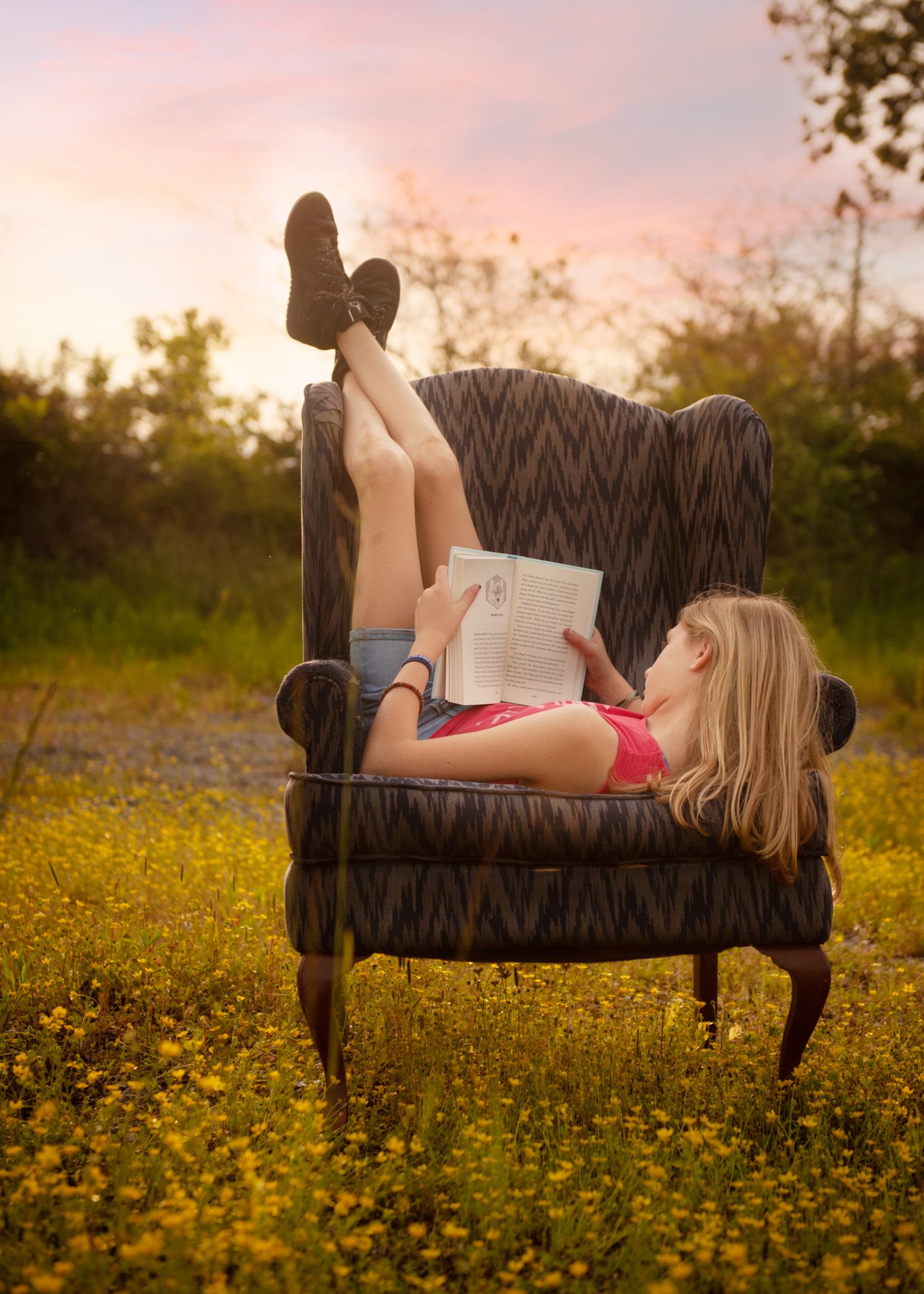 Someone relaxes on a vintage armchair in a field of yellow wildflowers at sunset.
