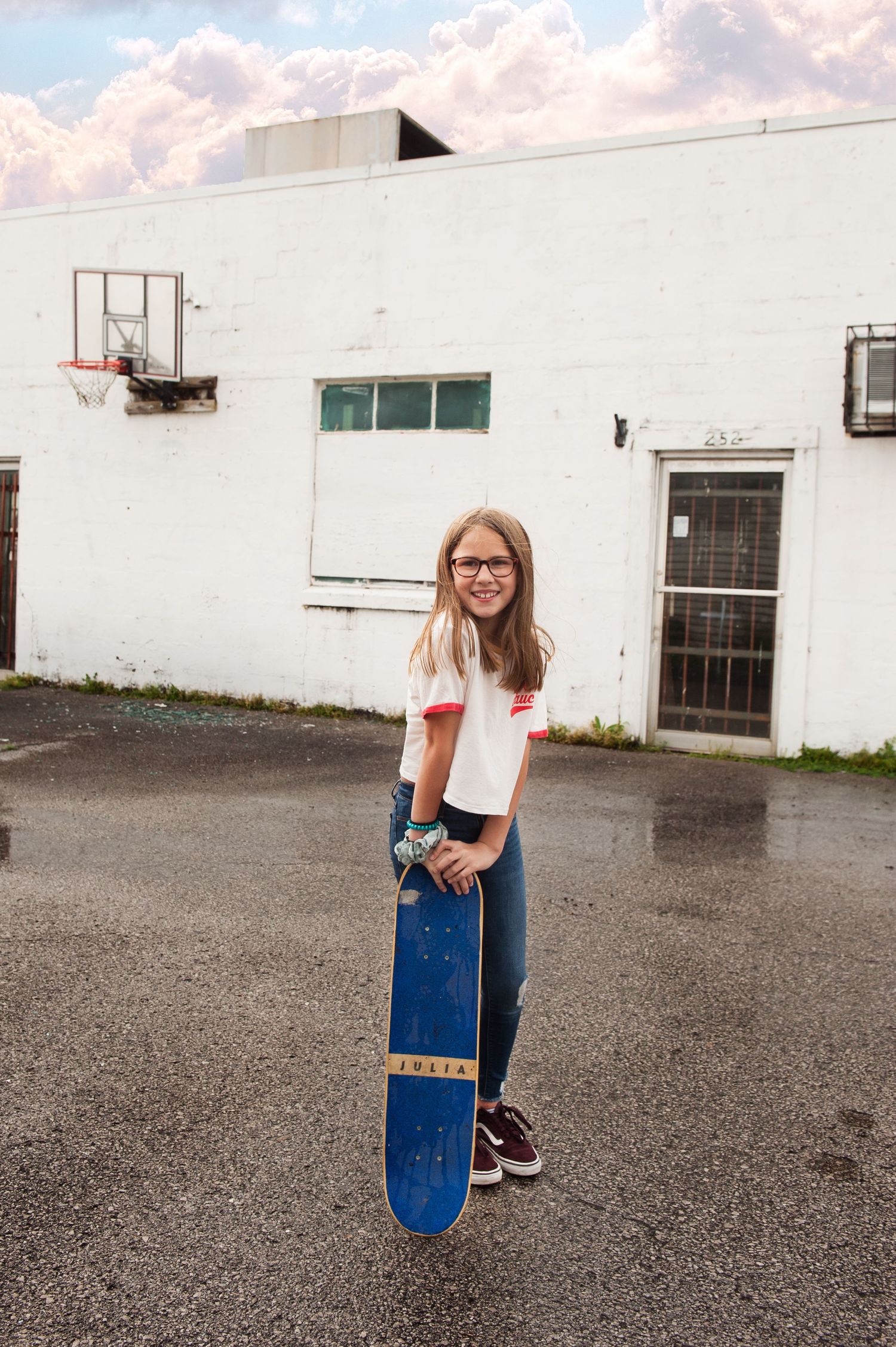 Portrait series of someone holding a blue skateboard in an outdoor parking lot.