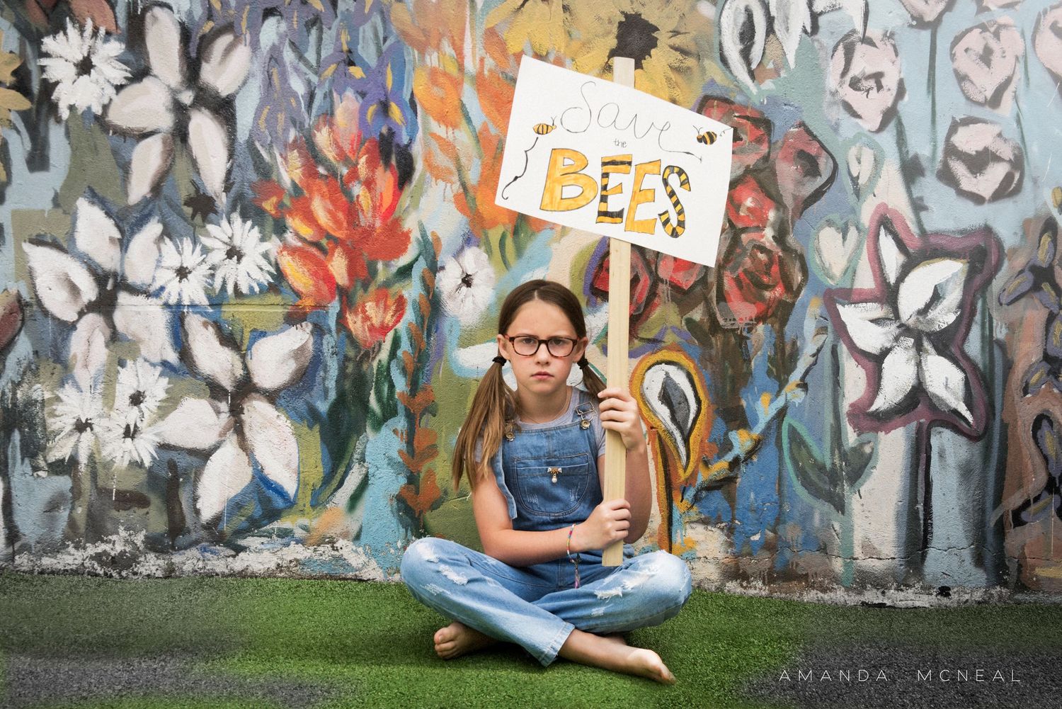 A child sits cross-legged holding a 'PETS' sign against a colorful floral mural background.