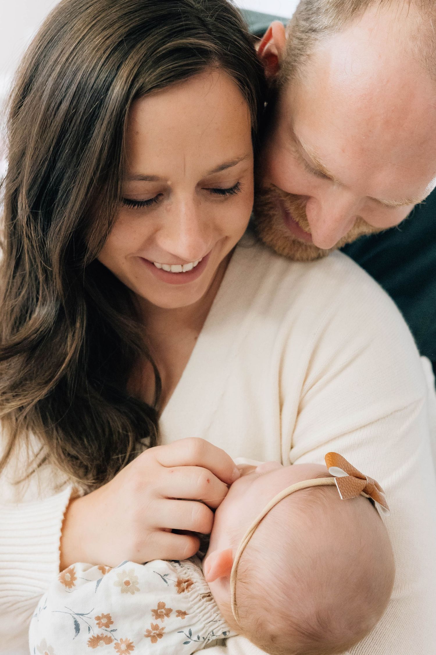 Loving parents smiling and gazing down at their newborn baby girl wearing a floral headband.