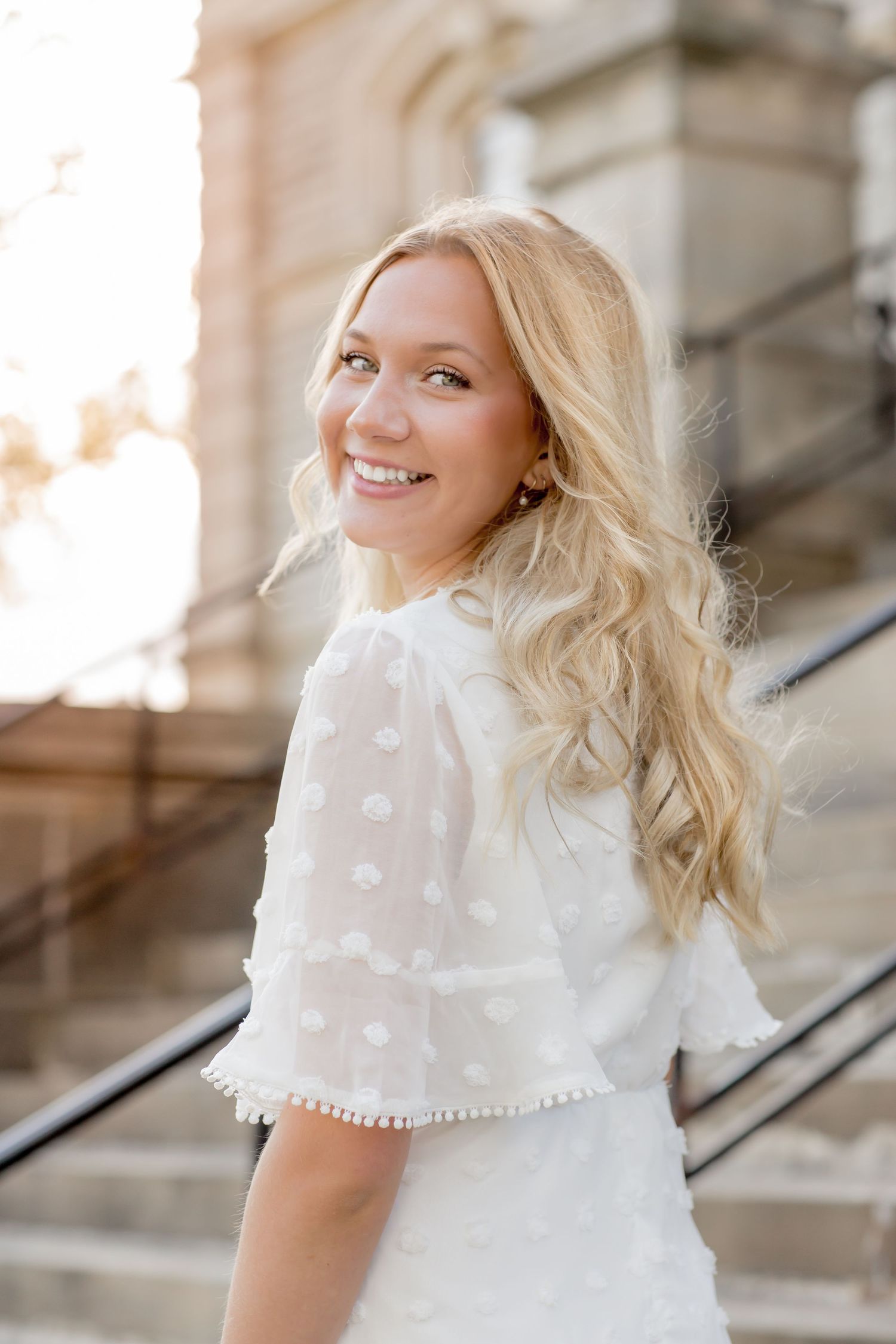 Smiling blonde young woman in a white polka dot top posing on outdoor stone steps.