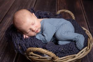 newborn baby in basket wearing blue laid on side