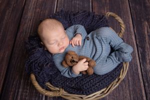 newborn baby in basket dressed in clue holding a brown teddy