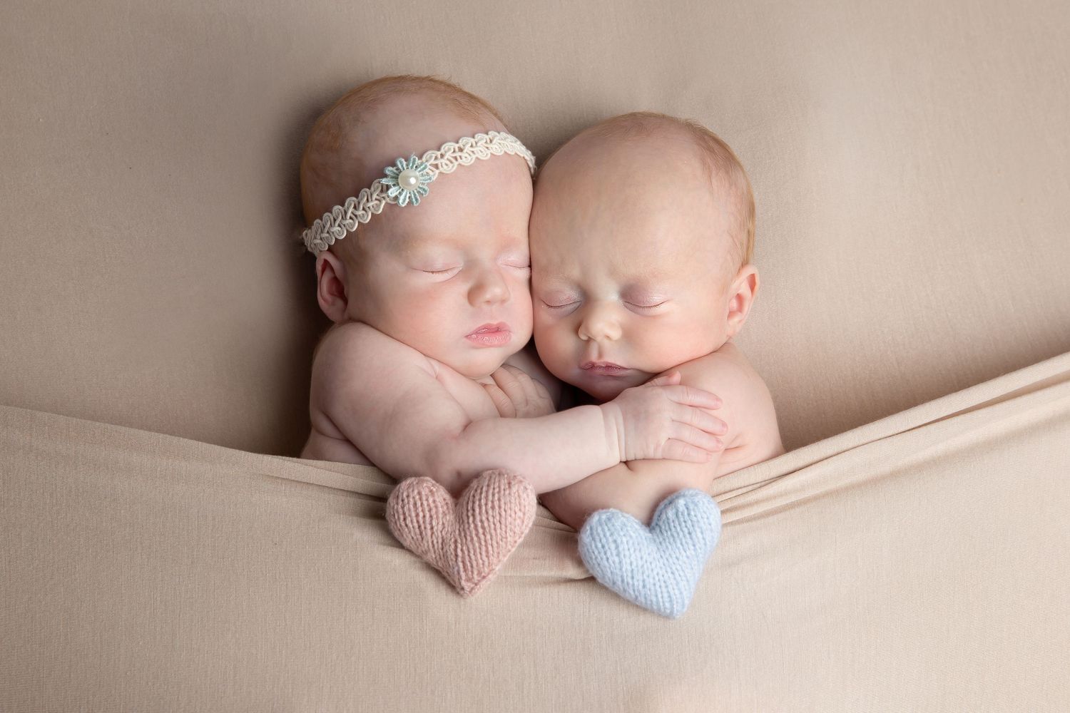 newborn twins hugging with a blue and pink heart