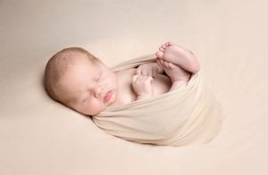 newborn baby curled up in cream wrap