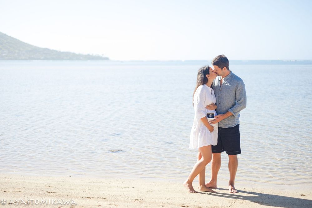 Romantic couple embracing on beach with calm ocean waters in background.