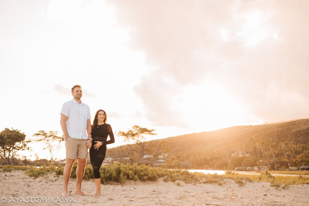 Couple standing on hillside during golden hour sunset with ocean view.