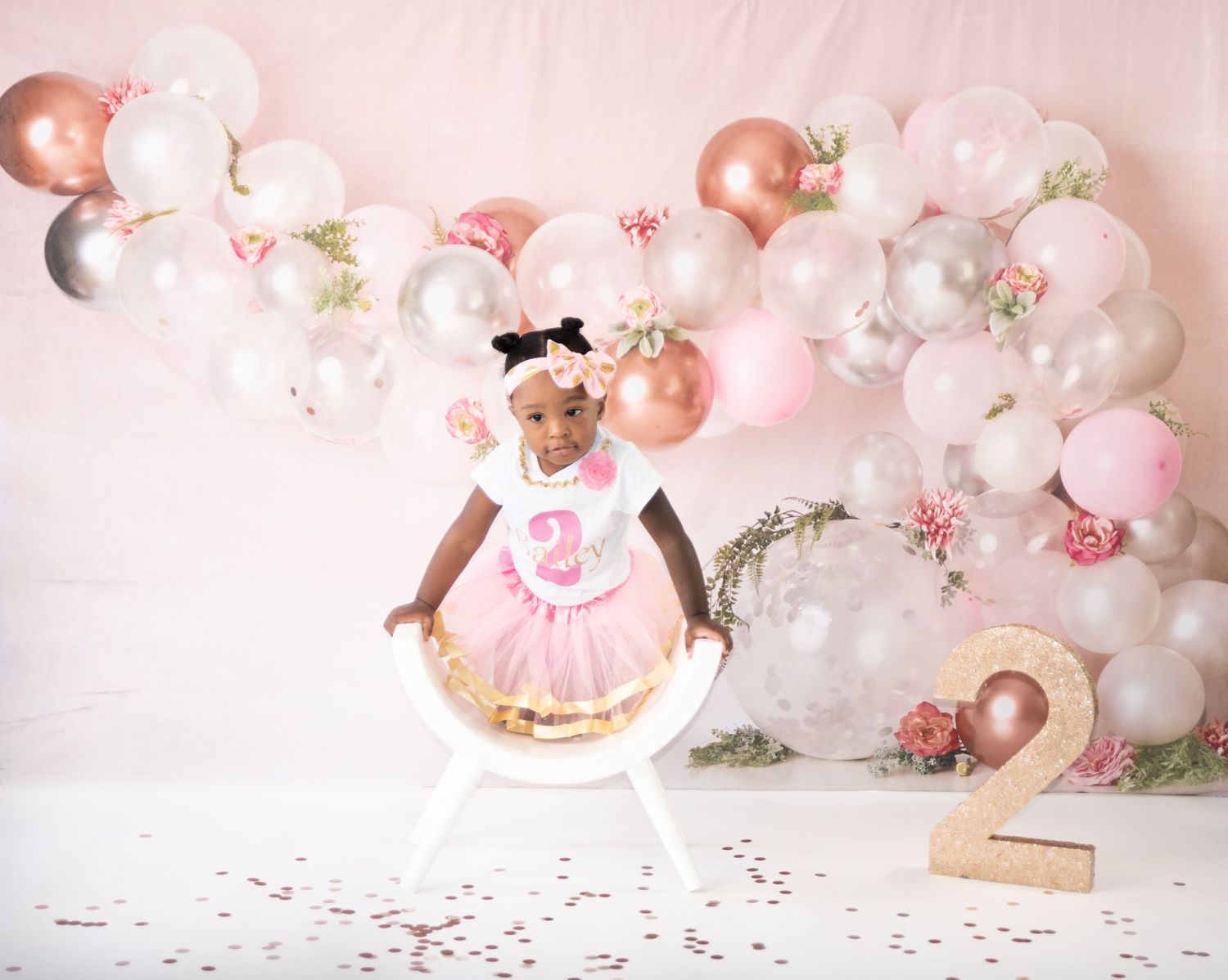 Pink and rose gold balloon arch with decorative floral accents for a birthday celebration setup.