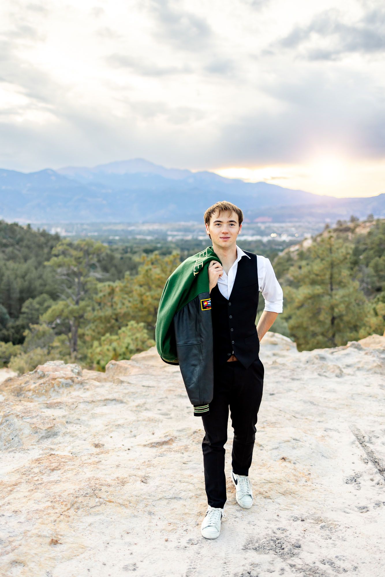 Senior guy walks and grins with his letter jacket over his shoulder at his senior session at Palmer Park in Colorado.
