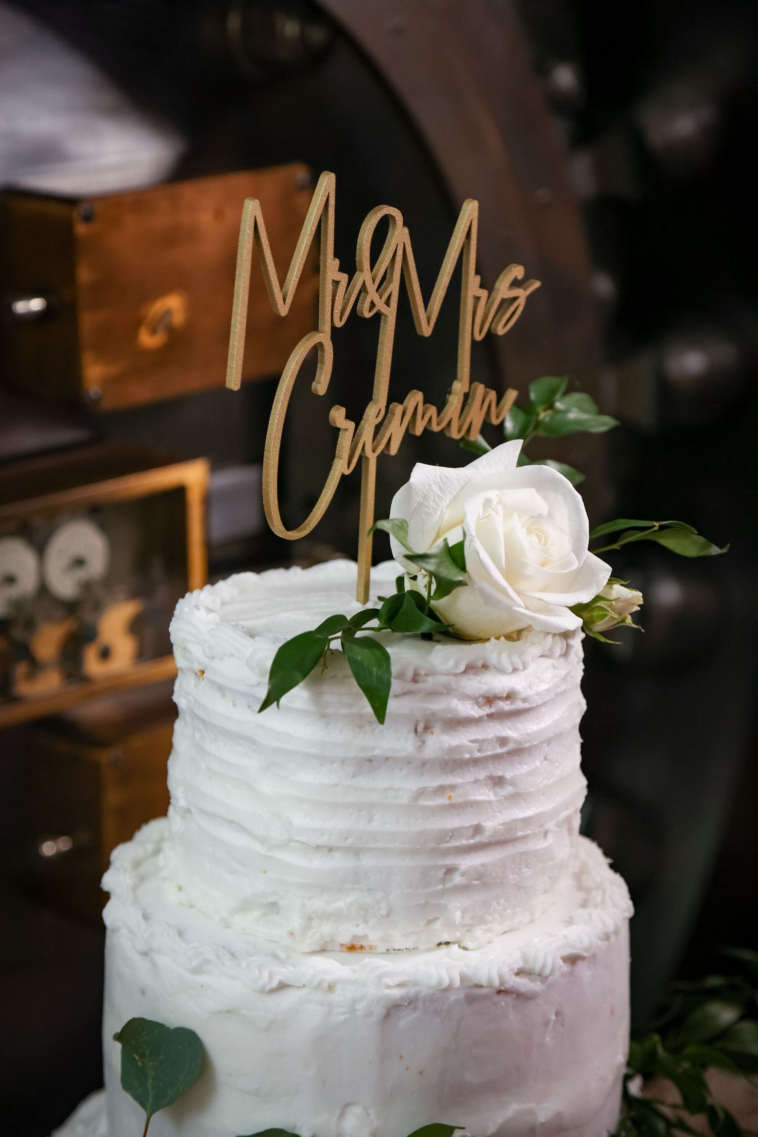 A white textured wedding cake decorated with fresh roses and a gold 'Mr & Mrs' topper.