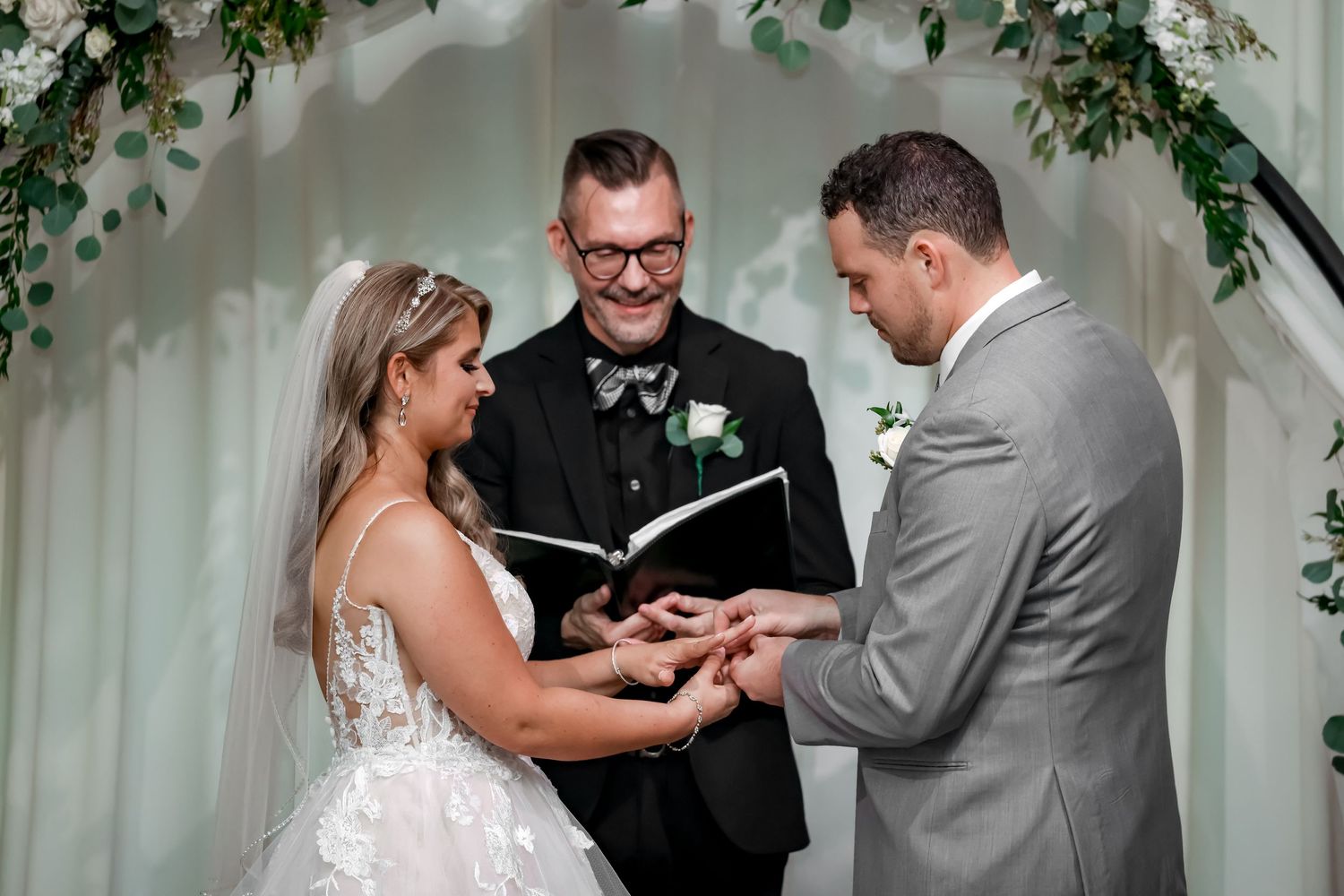 A wedding ceremony in progress with decorative greenery and white backdrop.
