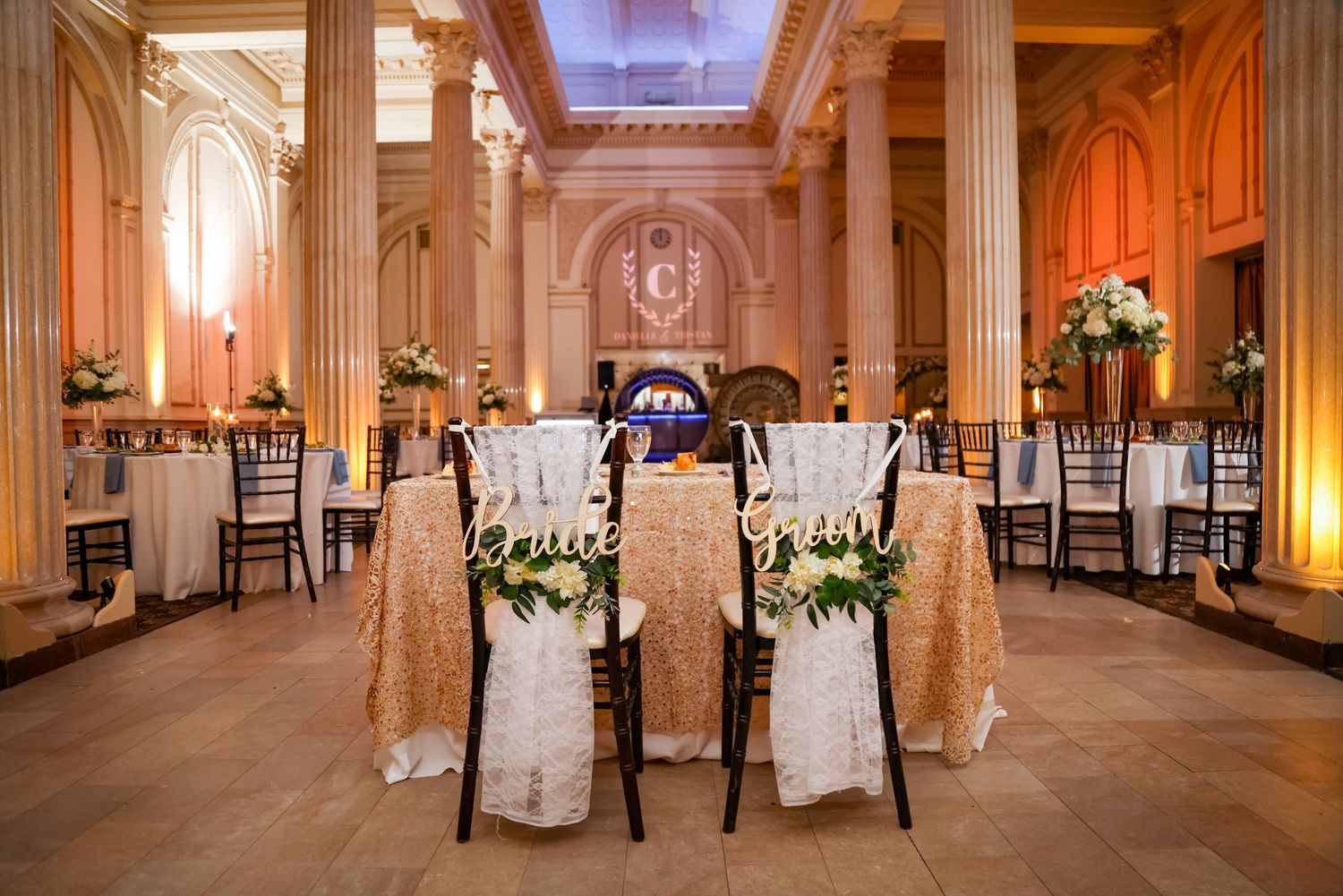 An elegant wedding reception setup in a grand hall with high ceilings and ornate architectural details.