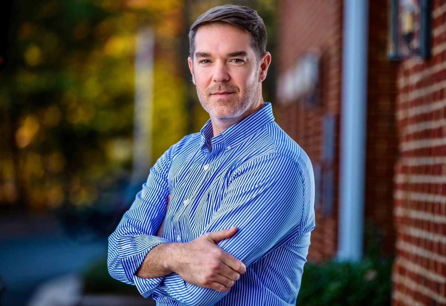 Professional headshot series of person in blue striped button-down shirt against brick wall.