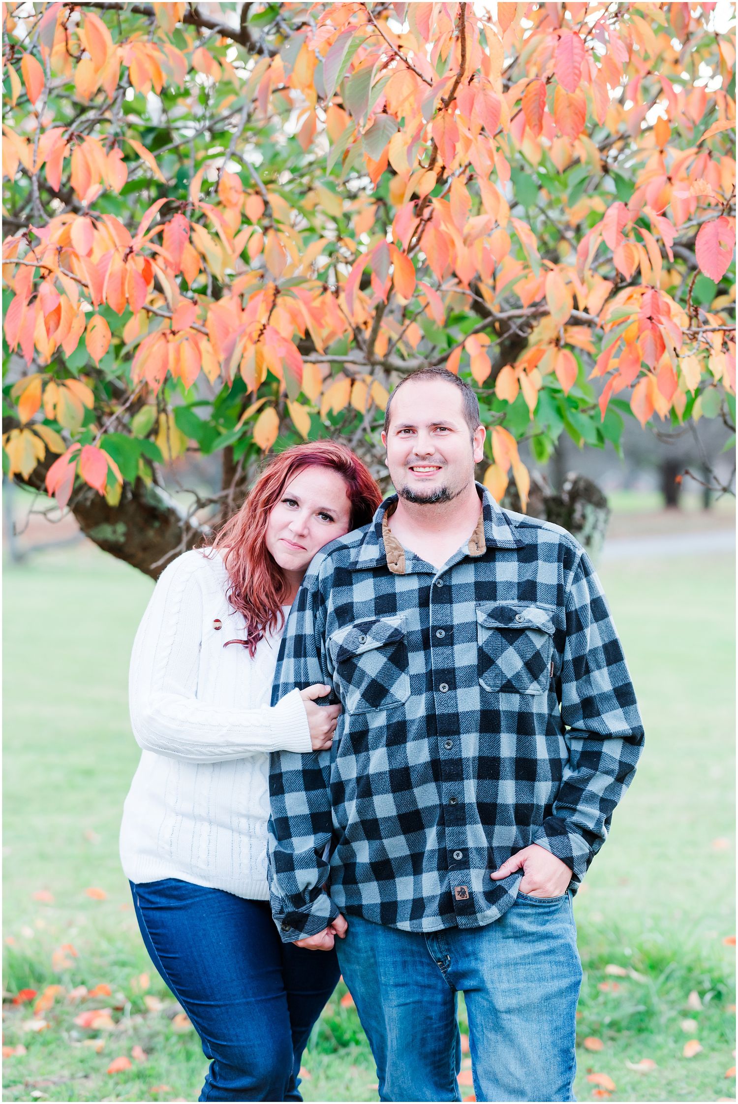Couple poses beneath orange autumn leaves wearing coordinating casual outfits.