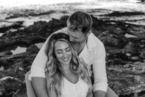 Couple embraces on rocky beach during outdoor photoshoot.